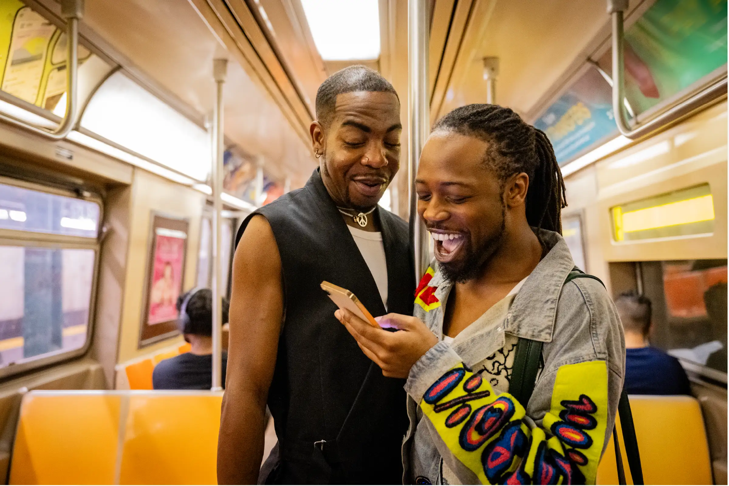 Two Guys on a train looking at a mobile phone laughing